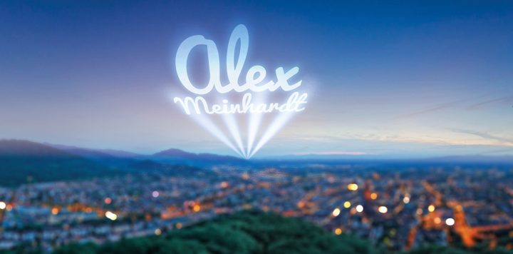 Motiv mit dem Namen „Alex Meinhardt“ im Bild: Name als Lichtprojektion über Stadt in der Abenddämmerung